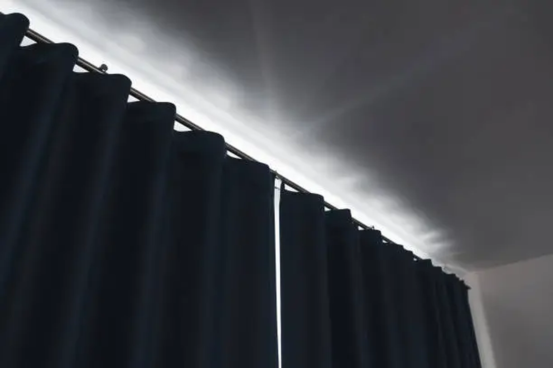 Dark blue eyelet curtain hanging from a ceiling-mounted track with light streaming across the ceiling